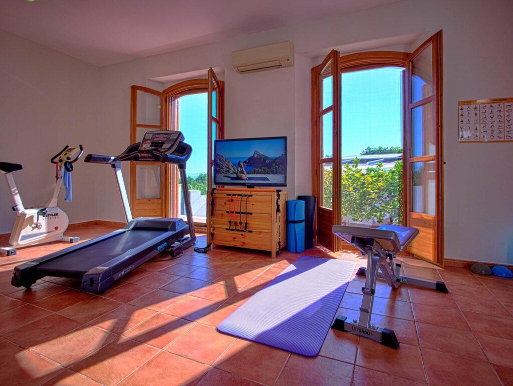 Luminoso gimnasio con cinta de correr, bicicleta estática y esterilla de yoga en el Cortijo El Sarmiento – ventanas en arco inundando el espacio de luz solar andaluza
