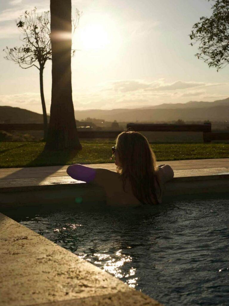 Huésped disfrutando de la piscina climatizada al atardecer en el Cortijo El Sarmiento – silueta bañada en luz dorada andaluza con vistas a las montañas