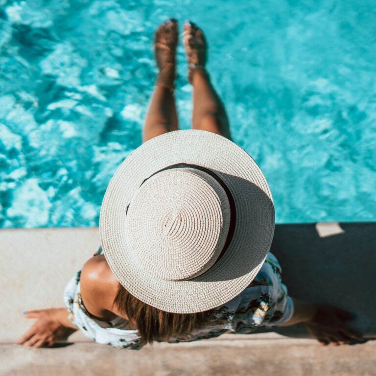 Wellness and Wellbeing: Unwind completely within our inviting wellness space - woman with a hat sitting relaxed by the pool